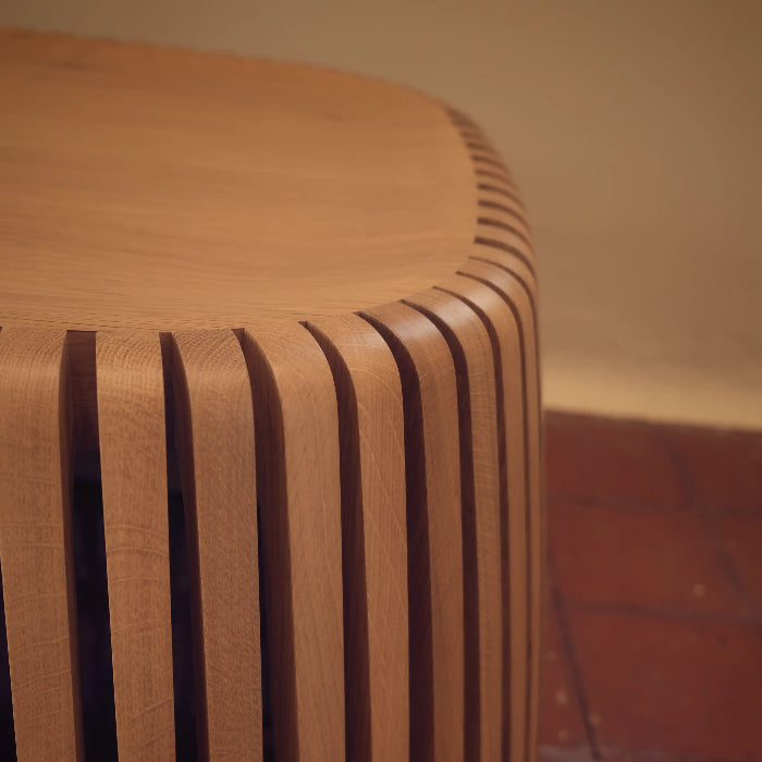 Wooden stool with a ribbed design on a red-tiled floor.