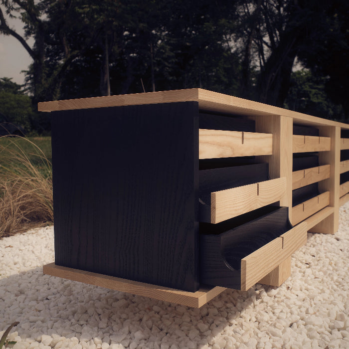 Wooden bench with black cushion on a gravel surface with trees in the background
