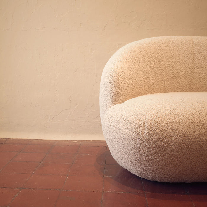 Beige textured chair against a plain wall with a red tiled floor.