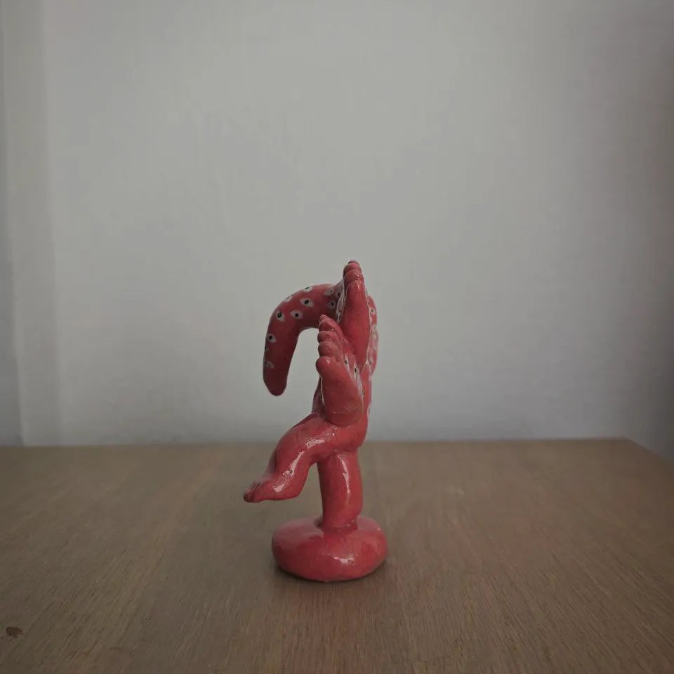 Red ceramic figurine on a wooden surface with a plain white background